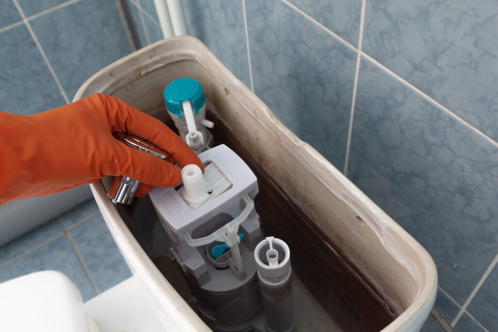A person fixing a toilet with the tank top off.