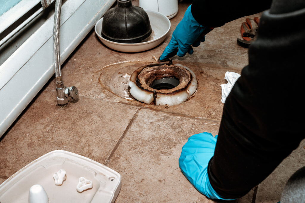Close-up image showing a plumber replacing the wax ring seal at the base of a toilet with copy space.